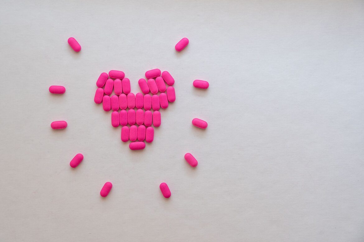 Pink pills arranged in a heart shape on a light surface, symbolizing health and care.