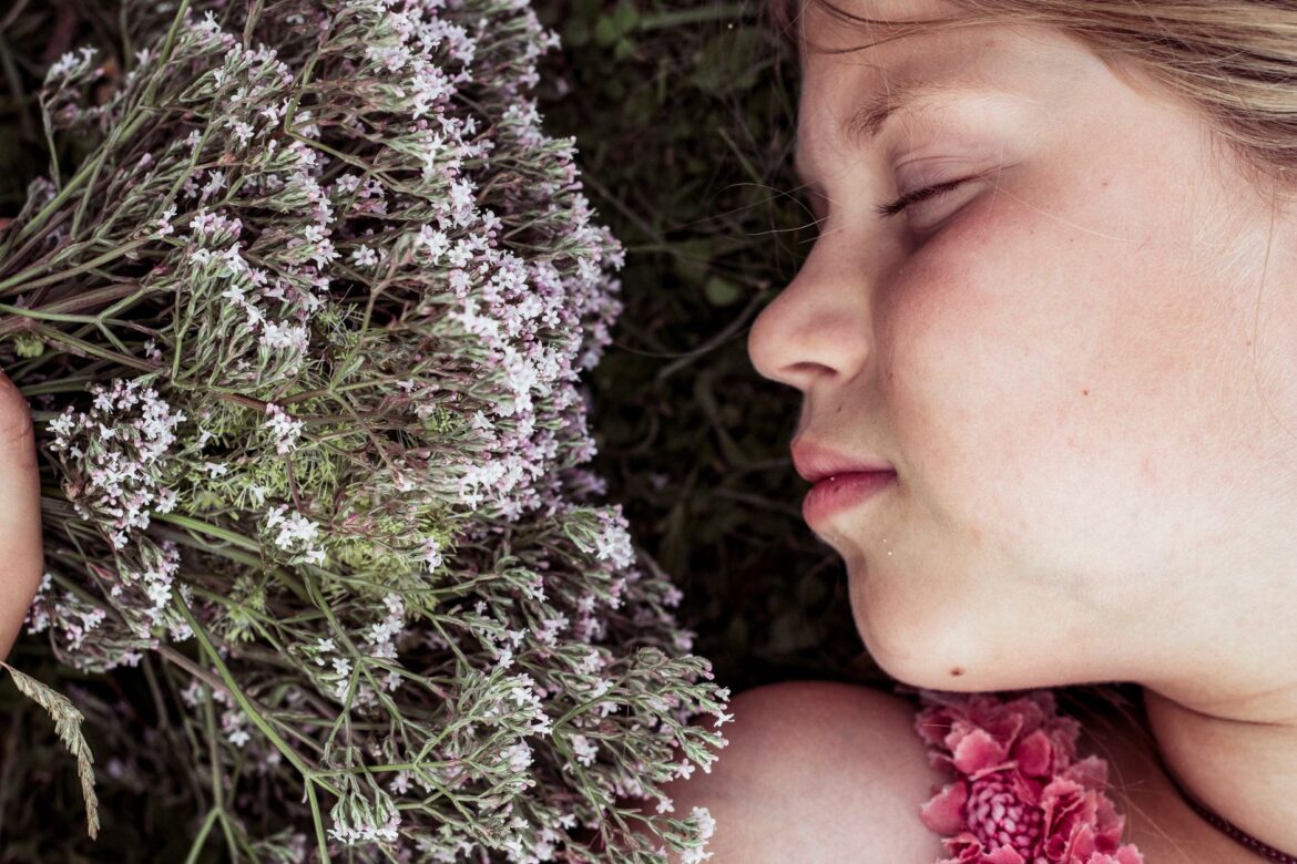A young girl with her eyes closed rests among blooming valerian flowers, radiating tranquility.