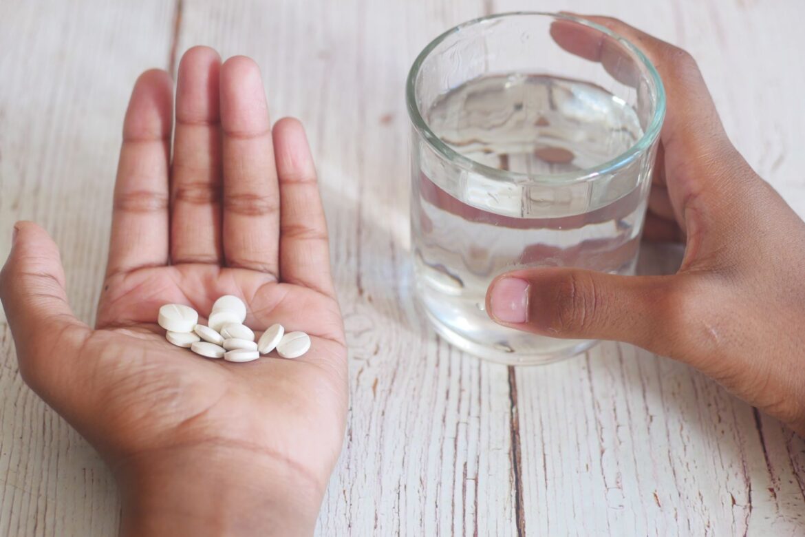 A close-up of hands holding medication tablets and a glass of water on a wooden surface.