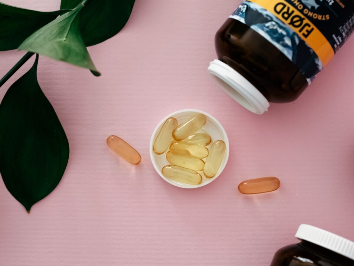 Top view of cod liver oil capsules in a bottle cap on a pink background.