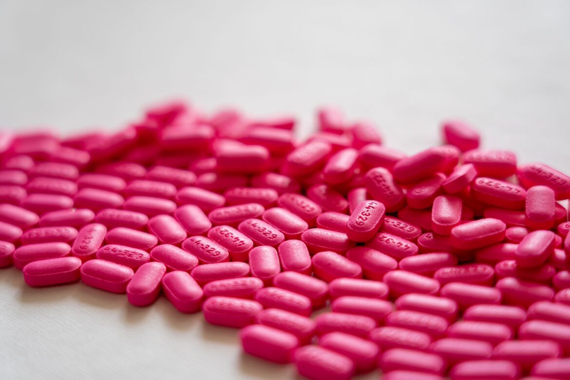 A detailed close-up of vibrant neon pink pills spread on a white table surface.