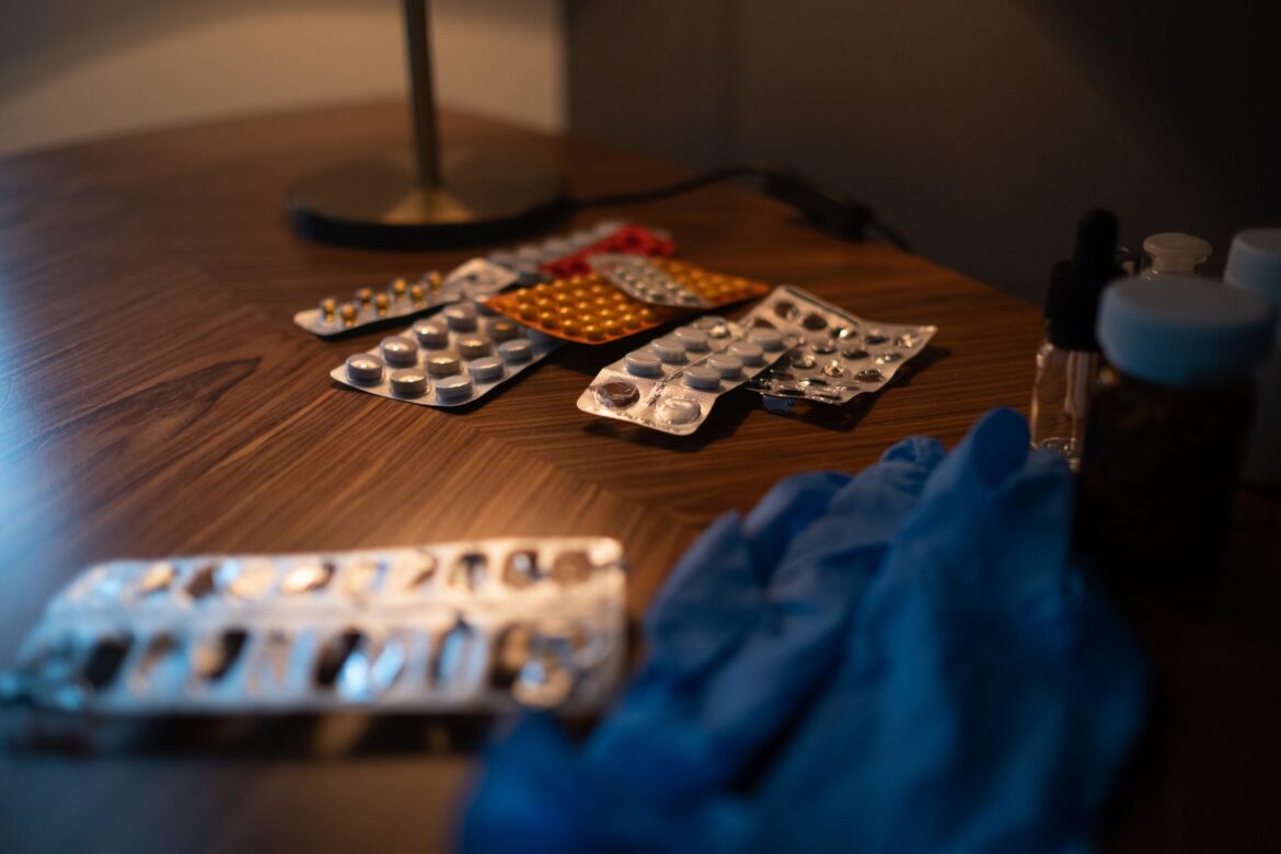 Close-up of various medication blister packs and gloves on a wooden table, signifying health and recovery.