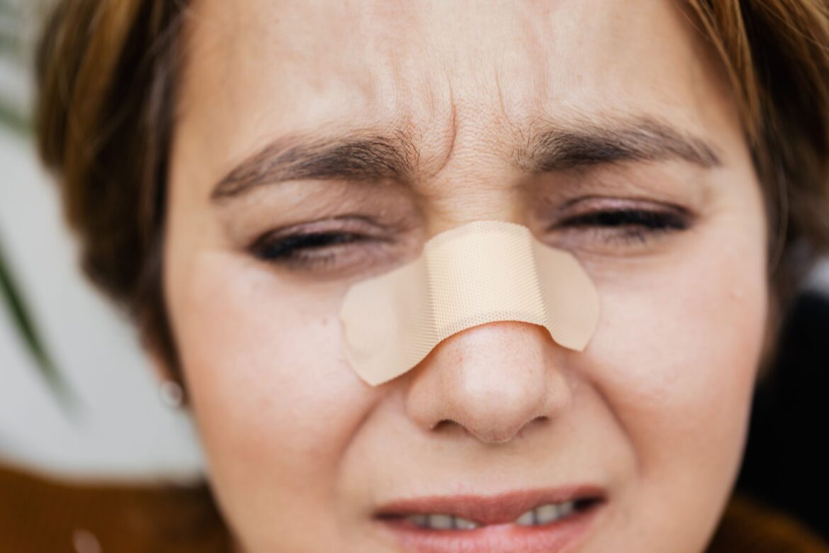 A close-up shot of a woman's face showing pain with a bandage over her nose.